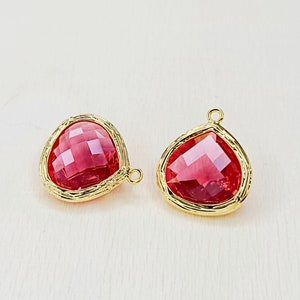 May include: Two gold-toned pendant charms with a red faceted glass stone in the centre. The stones are set in a gold-toned frame with a textured design.