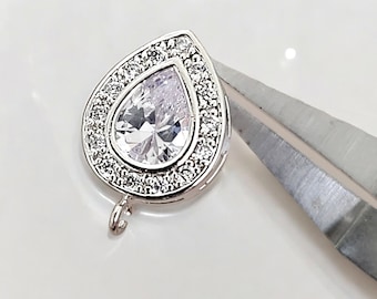 May include: A silver teardrop-shaped pendant with a clear crystal center surrounded by a halo of smaller crystals. The pendant has a loop at the bottom for attaching to a chain.