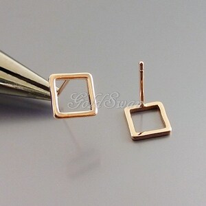 Könnte beinhalten: Ein Paar quadratische Ohrstecker aus Roségold. Die Ohrringe sind schlicht und minimalistisch, mit einem hohlen quadratischen Design.