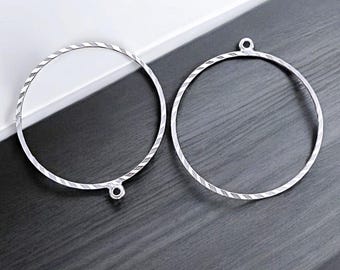 Puede incluir: Dos pendientes de aro de plata con un diseño texturizado. Los aros tienen un diámetro de aproximadamente 5 cm.