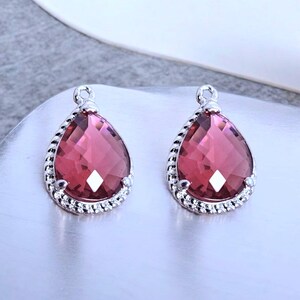 Peut inclure: Une paire de boucles d'oreilles en argent en forme de goutte avec un cristal rouge au centre. Les cristaux sont facetés et ont une bordure argentée.