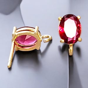 May include: A pair of gold-tone earrings with oval-shaped red gemstones. The earrings have a post back and a small loop on the top.