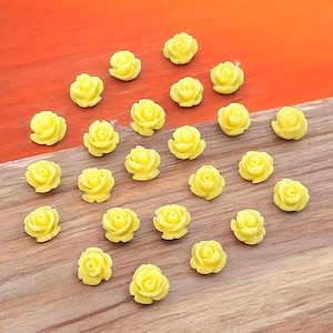 May include: A collection of 25 yellow rose-shaped resin embellishments. The embellishments are small and perfect for adding a touch of elegance to crafts and projects.