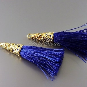 Op de afbeelding: Twee blauwe zijden kwastjes met gouden, kegelvormige metalen toppen. De toppen hebben een decoratief ontwerp met kleine blauwe steentjes.