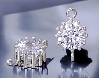 May include: Two silver-toned jewelry findings with clear crystal accents. Each finding features a round crystal surrounded by smaller crystals. One finding has a loop at the top, while the other has a side loop.