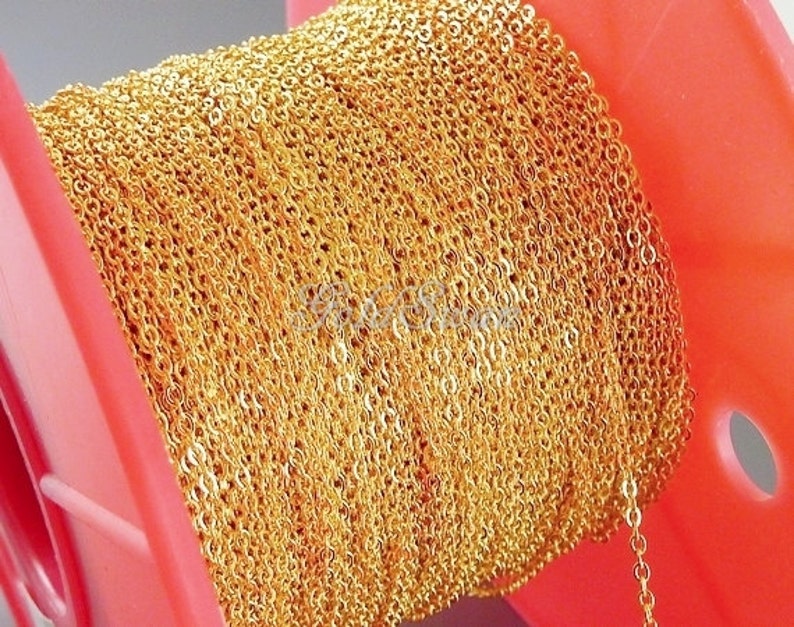 May include: A spool of gold-colored chain, wound tightly around a red plastic spool. The chain is made of small, linked circles.