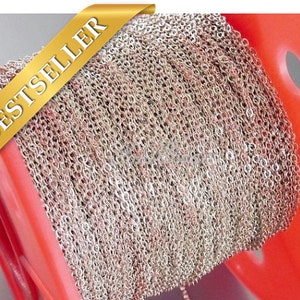 May include: A spool of silver chain, wound tightly, with a red plastic spool. The chain is a delicate, fine link chain.