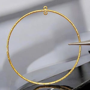 May include: A gold hoop earring with a small loop at the top for attaching to an earring post.