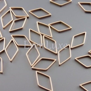 May include: A collection of small, gold-colored diamond-shaped metal frames scattered on a gray surface. The frames are open in the center and have a smooth, polished finish. These components could be used for jewelry making or other craft projects.
