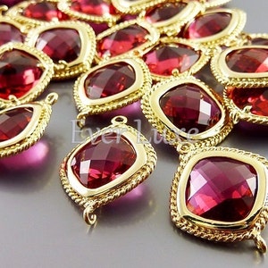 May include: A group of red crystal beads with gold-toned metal frames. The beads are square-shaped and have a faceted design. The beads have a loop on each side for stringing.