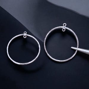 May include: Two silver hoop earrings with a textured finish. The hoops are different sizes and have a small loop at the top for attaching to a hook.
