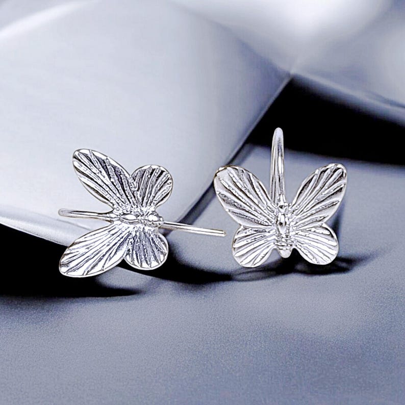 May include: A pair of silver butterfly earrings. The earrings are made of metal and have a detailed butterfly design.