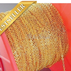 May include: A spool of gold-colored chain, wound tightly around a red plastic spool. The chain is a delicate, fine-link style.