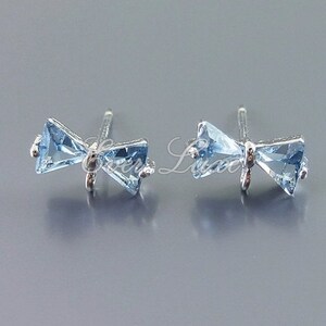 May include: A pair of silver bow-shaped earrings with light blue gemstone accents.