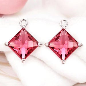 May include: A pair of silver earring charms with a square-shaped red gemstone.