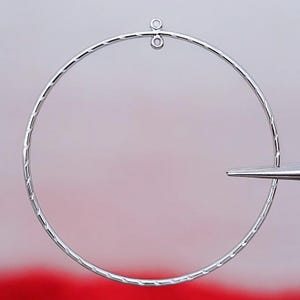 Peut inclure: Une boucle d'oreille en argent avec une surface texturée et une petite boucle en haut.