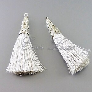 May include: Two white tassel pendants with silver metal caps. The caps have a decorative design.