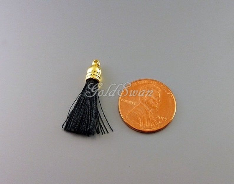 May include: A black tassel with a gold metal top. The tassel is about the size of a US penny.