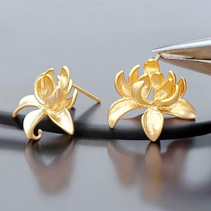 May include: A pair of gold-toned earrings featuring a detailed lotus flower design. The earrings are made of metal and have a post back closure.