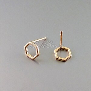 May include: A pair of gold hexagon stud earrings. The earrings are simple and minimalist, with a geometric design.