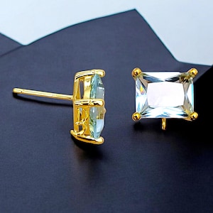 Puede incluir: Un par de pendientes de oro con piedras preciosas cuadradas transparentes. Los pendientes tienen un cierre de poste.