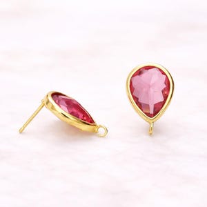 May include: A pair of gold-colored stud earrings with a teardrop-shaped, faceted, pink gemstone. The earrings have a gold bezel setting and a post for pierced ears. The gemstone is a vibrant shade of pink.