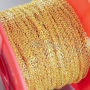 May include: A spool of gold-colored chain, wound tightly around a red plastic spool. The chain is made of small, linked circles.