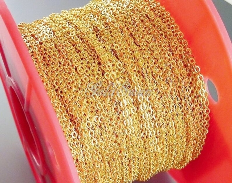 May include: A spool of gold-colored chain, wound tightly around a red plastic spool. The chain is made of small, linked circles.