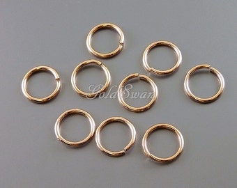 May include: Eight gold jump rings, also known as split rings, are arranged on a gray surface. These rings are commonly used in jewelry making and crafting.