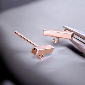 May include: Two rose gold bar earring findings with jump rings. The findings are rectangular and have a smooth, polished finish.