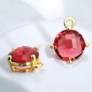May include: Two gold-tone charms with a red faceted gemstone. Each charm has a loop for attaching to a necklace or bracelet.