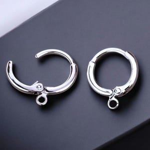 May include: Two silver-toned earring hoops with a hinged clasp. The hoops are smooth and have a polished finish.
