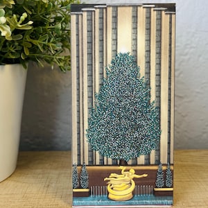 Puede incluir: Una impresión artística rectangular con temática navideña que presenta una ilustración detallada de un árbol de Navidad decorado, una escultura dorada y una fachada de edificio. La obra de arte tiene una combinación de colores verde azulado y dorado, con un enfoque en la decoración navideña.