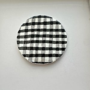 May include: A round ceramic coaster with a black and white checkered pattern.