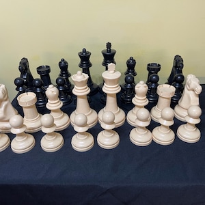 May include: A complete chess set with black and off-white pieces. The pieces are arranged on a dark surface, showcasing the king, queen, rook, knight, bishop, and pawns. The set is ready for a game of strategy.