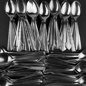 May include: A monochrome image showcasing a collection of spoons. The spoons are arranged in two sections, with the top group standing vertically and the bottom group lying horizontally. The spoons feature diverse handle patterns.