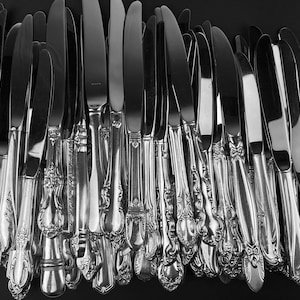 Peut inclure: Gros plan sur un groupe de couteaux à dîner en argent avec des manches ornés. Les couteaux sont disposés en un motif vertical, les lames pointant vers le haut.