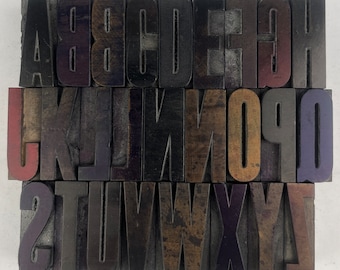 Può includere: Un set di blocchi di stampa tipografica in legno vintage, che presentano l'alfabeto dalla A alla Z. I blocchi sono in legno scuro e hanno un aspetto usurato e antico. Ogni lettera è scolpita individualmente e ha un carattere distintivo.