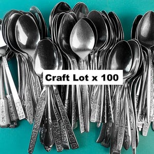 May include: A large assortment of vintage silver spoons, set against a teal backdrop. The spoons, with diverse patterns, are densely packed. The text "Craft Lot x 100" is displayed on a white rectangle.