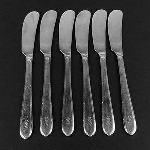 May include: Set of six silver butter knives with ornate handles. The knives have a simple, elegant design.