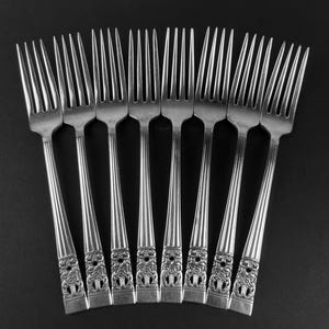 May include: A set of silver forks displayed on a dark background. The forks have ornate floral detailing on the handles and a traditional design. The tines are long and slender, and the forks are arranged in a fan shape.