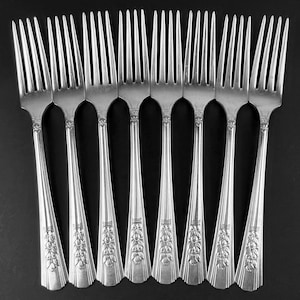 May include: Eight silver forks with ornate floral designs on the handles. The forks are arranged in a row, with the tines facing upwards.