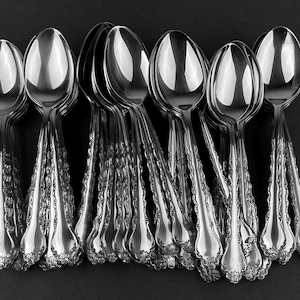 May include: A set of silver spoons with ornate handles. The spoons are arranged in a row, with the handles facing the viewer. The spoons are all polished and shiny.