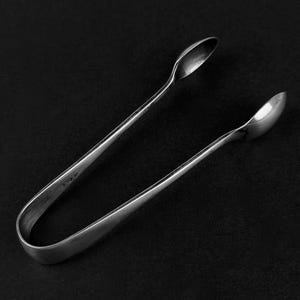 May include: Silver sugar tongs with a simple design. The tongs are made of polished metal and have a slight curve to them.