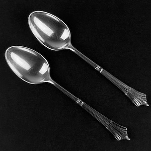 May include: Two silver spoons with ornate handles. The spoons are lying on a black surface.