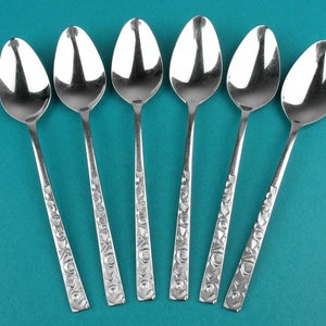 Peut inclure: Six cuillères en argent avec des motifs ornés sur un fond bleu sarcelle.