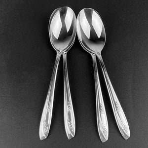 May include: Four silver spoons with ornate floral designs on the handles. The spoons are arranged in a group with the handles pointing upwards.