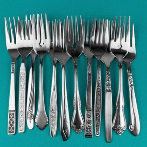 May include: A set of ten silver forks with ornate handles. The forks are arranged in a row on a teal background.