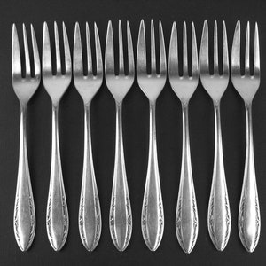 May include: A set of ten silver forks with ornate designs on the handles. The forks are arranged in a row on a black surface.