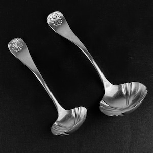 May include: Two silver serving ladles with ornate handles and a scalloped bowl shape.